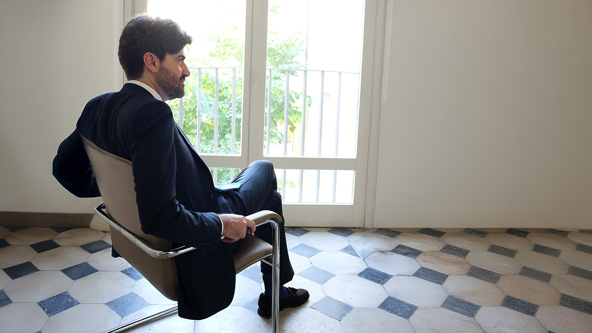 Andrea Iosa di profilo vicino alla finestra con abito gessato blu su misura